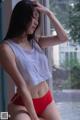 A woman in a white tank top and red panties sitting on a window sill.