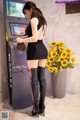 A woman in a black dress and thigh high boots standing next to a vending machine.