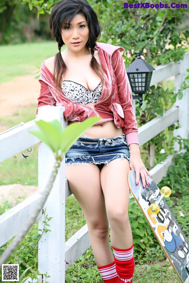 A woman sitting on a fence holding a skateboard.